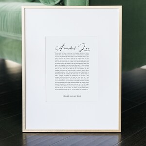 Pu&ograve; includere: Una stampa incorniciata con sfondo bianco e sovrapposizione di testo nero. Il testo recita "Annabel Lee" e include una poesia di Edgar Allan Poe. La cornice &egrave; in legno chiaro.