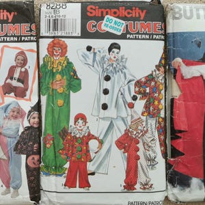 May include: Three sewing pattern envelopes for costumes. The left envelope is Simplicity 7984 featuring various children's outfits. The centre envelope is Simplicity 8288 showing clown costumes. The right envelope is Butterick 4971 displaying vampire attire.
