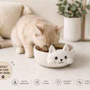 May include: A round, off-white ceramic pet bowl featuring a sculpted cat face with ears and paws extending from the rim. The bowl contains brown dry food pellets. Text on the image includes "PERFECT FOR YOUR FURRY FRIEND," "DIGITAL DOWNLOAD," "EASY TO MAKE," "BEGINNER FRIENDLY," and "PERFECT FOR SLAB POTTERY."