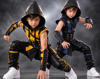 Può includere: Due costumi con cappuccio in combinazioni di colori nero e giallo o nero e blu. Ogni completo include una tunica senza maniche, pantaloni abbinati, protezioni per le braccia con lacci e una cintura con fibbie, indossati con scarpe da ginnastica bianche.
