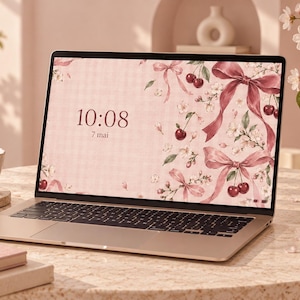 Peut inclure: Un ordinateur portable avec un fond d'écran rose clair orné d'un motif de cerises rouges, de fleurs blanches et de rubans roses. L'écran affiche l'heure 10:08 et la date 7 mai en police sombre. L'ordinateur a une finition argentée et des touches noires.