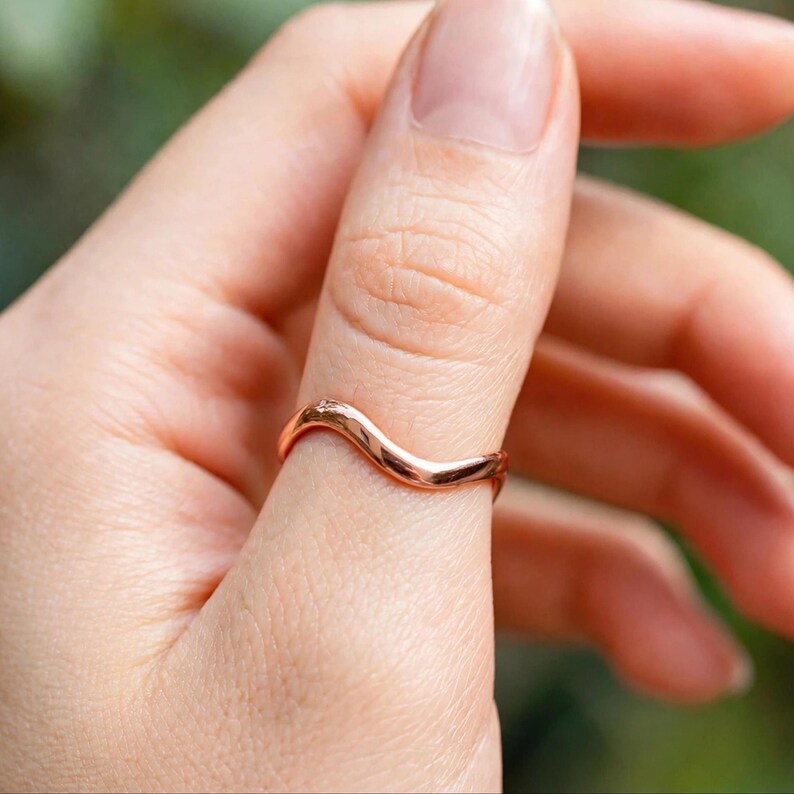 Handmade rose gold vermeil wave ring over sterling silver organic wavy band on white textured stone surface luxury minimal top view, thin polished curved ripple contour high mirror shine chevron bypass stacking band, modern boho ocean wave wishbone ring for women rose gold plated surf inspired everyday jewelry Jaipur artisan handmade rose gold wave ring gift for her