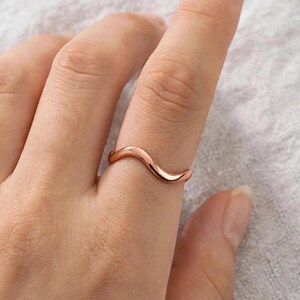 Handmade pure solid copper wave ring on index finger close-up natural skin texture detail light linen background minimalist lifestyle, thin organic wavy contour band polished curved ripple bypass design high mirror shine chevron stacking, modern boho ocean wave wishbone ring for women solid unplated copper everyday jewelry Jaipur artisan handmade pure copper ring gift for her beach lover