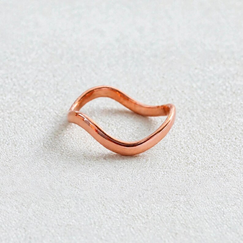 Handmade pure copper wave ring organic wavy band on off white textured surface natural unplated copper metal top view, solid copper thin polished curved ripple contour high shine chevron bypass stacking band, minimalist boho ocean wave wishbone ring for women pure copper surf inspired everyday jewelry Jaipur artisan handmade solid copper wave ring hypoallergenic gift for her