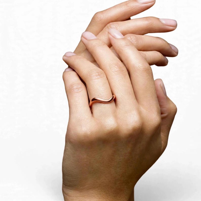 Handmade pure solid copper wave ring on middle finger woman both hands clasped together white studio background natural bare pink nails elegant pose, thin organic wavy bypass contour band unplated copper high mirror polish ripple chevron stacking minimalist boho ocean wave wishbone ring for women dainty surf inspired everyday jewelry Jaipur handmade pure copper clasped hands gift