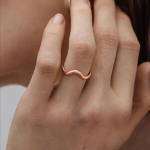 Handmade pure copper rose gold tone wave ring on middle finger woman touching neck ear side face close-up brown hair natural bare nails gold chain necklace background, thin organic wavy bypass contour high mirror shine polished ripple chevron stacking band minimalist boho ocean wave wishbone ring for women dainty surf inspired everyday jewelry Jaipur handmade pure copper gift