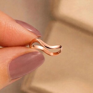 Handmade rose gold plated sterling silver wave ring held between thumb index finger mauve purple nail polish manicure extreme macro beige bokeh close-up, thin organic wavy contour bypass band high mirror polish ripple chevron stacking curve light reflection, minimalist boho ocean wave wishbone ring for women dainty surf everyday jewelry Jaipur handmade rose gold nail art display gift for her
