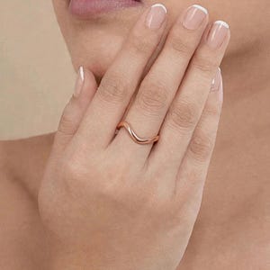 Handmade rose gold plated sterling silver wave ring on middle finger woman French manicure hand near chin lips beige background elegant close-up, minimalist thin wavy contour band polished ripple chevron bypass stacking design high mirror shine, modern boho ocean wave wishbone ring for women rose gold surf inspired everyday jewelry Jaipur handmade delicate rose gold ring gift for her