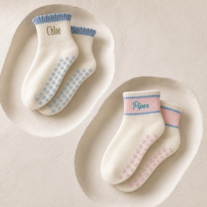 Puede incluir: Dos pares de calcetines tobilleros. Un par es color crema con puño acanalado azul y el nombre Chloe bordado en marrón. El otro par es color crema con puño a rayas rosa y azul y el nombre Piper bordado en azul. Ambos tienen suelas antideslizantes.
