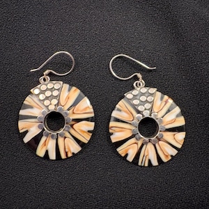 Peut inclure: Une paire de boucles d'oreilles pendantes circulaires avec un motif radial de segments crème, beige et noir. Chaque boucle possède un centre en métal argenté avec une petite découpe circulaire, une partie supérieure triangulaire texturée à pois.