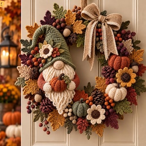 May include: A circular autumn wreath featuring a crocheted gnome wearing a green hat, holding a small orange pumpkin. The wreath is decorated with crocheted leaves in shades of yellow, orange, and burgundy, pinecones, berries, and a hessian bow.