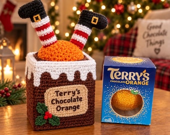 Puede incluir: Una funda de chimenea de ganchillo marrón con borde blanco, hojas de acebo verdes y bayas rojas, con dos piernas con botas negras y calcetines a rayas rojas y blancas, junto a una caja azul de Terry's Chocolate Orange.