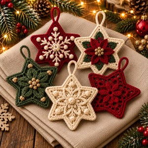 Op de afbeelding: Vijf stervormige gehaakte ornamenten met ingewikkelde ontwerpen. Eén is donkerrood met een witte sneeuwvlok, één is crème met een rode en groene kerstster, één is donkergroen met gouden accenten, één is crème met een bloemmotief en één is rood.