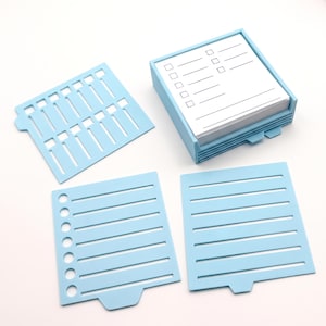 May include: A light blue plastic memo pad holder containing a stack of white paper with printed checklists, accompanied by three distinct light blue plastic stencils featuring various line and checkbox patterns for organizing notes and tasks.