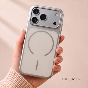 Könnte beinhalten: Eine silberfarbene Smartphone-Hülle mit transparenter Rückseite, die einen kreisförmigen magnetischen Ladering und eine vertikale Liniengrafik aufweist. Die Hülle enthält einen erhöhten rechteckigen Kameraausschnitt und den Markennamen POUCHORA.