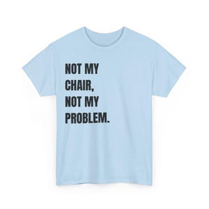 May include: A light blue short-sleeved t-shirt featuring the black text "NOT MY CHAIR, NOT MY PROBLEM." printed on the front. The garment has a crew neckline and a standard fit, showcasing a simple design with bold, sans-serif lettering.