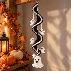 May include: A hanging crochet decoration featuring a long, spiraling black and white striped ribbon. Attached to the spiral are five small white crocheted ghosts with black eyes and mouths, with a larger white ghost at the bottom.