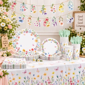 May include: A party supply set featuring a white tablecloth, plates, cups, and napkins decorated with colorful watercolor wildflowers and butterflies. Includes a hanging banner of floral cutouts, light green plastic forks and spoons, and a sign.
