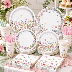 May include: A party supply set featuring white paper plates, cups, and napkins decorated with a colorful wildflower meadow pattern, small butterflies, and dragonflies. The set includes stacks of plates, cups filled with pink plastic forks, and napkins.