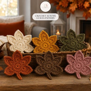 May include: Six crocheted autumn leaves in cream, yellow, olive green, orange, brown, and dusty pink, arranged in a woven basket. The leaves feature a circular center with radiating petal-like points. Text reads: CROCHET AUTUMN LEAVES PATTERN.