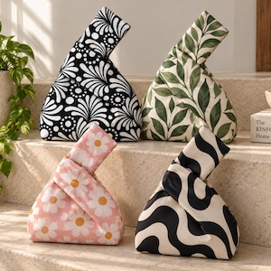 Puede incluir: Cuatro bolsos de tela con nudo y patrones distintos: uno floral en blanco y negro, uno con estampado de hojas verdes, uno rosa con margaritas blancas y uno con rayas onduladas en blanco y negro. Cada bolso tiene forma triangular y un asa anudada.