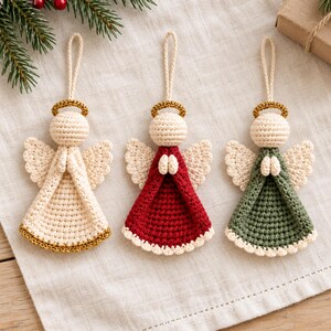 May include: Three crocheted angel ornaments with hanging loops. One is cream with a gold halo and hem, one is red with a gold halo and cream wings, and one is sage green with a gold halo and cream wings. Each angel has hands clasped in front.