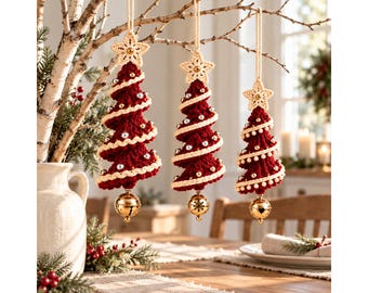 May include: Three hanging Christmas tree ornaments crafted from deep red yarn with a spiral cream-coloured trim. Each tree is topped with a crocheted star, decorated with small silver beads, and features a shiny gold jingle bell at the bottom.