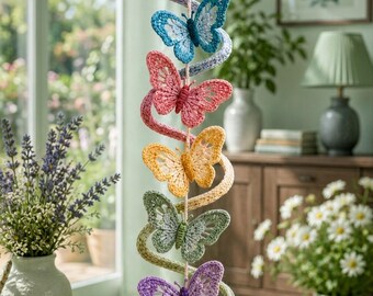 May include: A vertical hanging mobile featuring six crocheted butterflies in purple, blue, pink, yellow, green, and light purple. The butterflies are connected by a spiraling yarn strand and a central cord, finished with a clear crystal prism at the bottom.