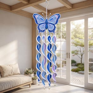 May include: A hanging crochet butterfly mobile featuring a large blue, light blue, and lavender butterfly at the top. Four long, spiraling crochet ribbons in matching blue and lavender shades hang from the butterfly, each finished with a small white bead.