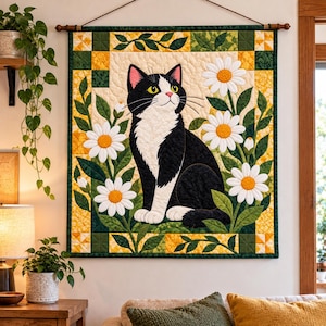 Puede incluir: Un tapiz de pared rectangular de tela que presenta un gato esmoquin blanco y negro sentado entre margaritas blancas con centros amarillos. El edredón tiene un borde de patrones geométricos verdes y amarillos.