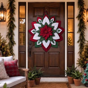 May include: A large, multi-layered fabric poinsettia wall hanging featuring pointed petals in shades of deep red, forest green, and white, centered with small red berries, displayed as a decorative accent on a dark wooden front door.
