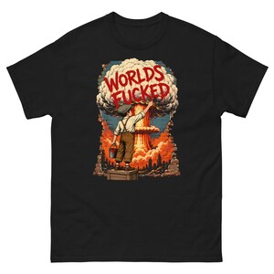 May include: A black t-shirt featuring a graphic of a child standing on a crate, painting the words WORLDS FUCKED in red onto a brick wall. Behind the wall, a large mushroom cloud rises over a city skyline in shades of orange and blue.