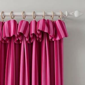 Op de afbeelding: Een gordijn met verticale strepen in afwisselende tinten donkerroze en lichtroze. De stof is aan de bovenkant geplooid met lichtgekleurde houten ringen die langs een witte gordijnroede met decoratieve eindknoppen schuiven.