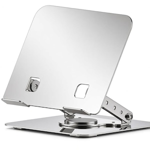 Puede incluir: Un soporte para portátil de metal plateado con un acabado pulido y reflectante. El soporte cuenta con una base cuadrada, un mecanismo giratorio central y un brazo de soporte ajustable con múltiples ranuras para la altura.