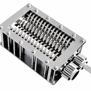Puede incluir: Un mecanismo triturador industrial de color plateado con un marco metálico rectangular y múltiples cuchillas giratorias internas. El dispositivo incluye dos engranajes externos y un eje de transmisión que sobresale, asegurado con pernos.