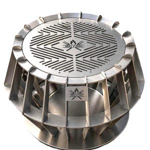 Może przedstawiać: Okrągły grill ze stali nierdzewnej z geometryczną, szczelinową powierzchnią górną i pionową podstawą z żebrami. Środek góry oraz mała prostokątna płytka z boku są wygrawerowane napisem GRILL & CHILL oraz ikoną płomienia.