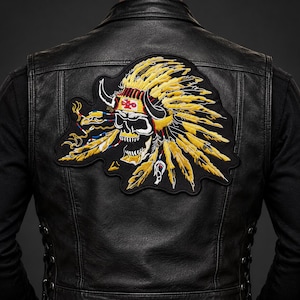 May include: A black leather vest featuring a large embroidered patch on the back. The patch depicts a skull wearing a yellow feathered headdress with black horns, accented with red and white details, centered on a black fabric background.