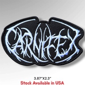 May include: An oval-shaped embroidered patch with a black background and white stylized lettering that reads CARNIFEX. The patch features a jagged, branch-like font design and measures 3.87 inches by 2.3 inches as indicated by the text below.