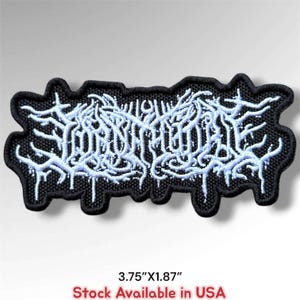May include: A black embroidered patch featuring intricate, light blue, stylized lettering with a jagged, branch-like design. The patch has a black border and measures 3.75 inches by 1.87 inches, as indicated by the text below the item.