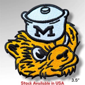 May include: An embroidered patch featuring a yellow and black stylized animal head wearing a light blue pot with a black letter M on the front. The patch measures 3.5 inches in height and width, with thick black stitching outlining the design.