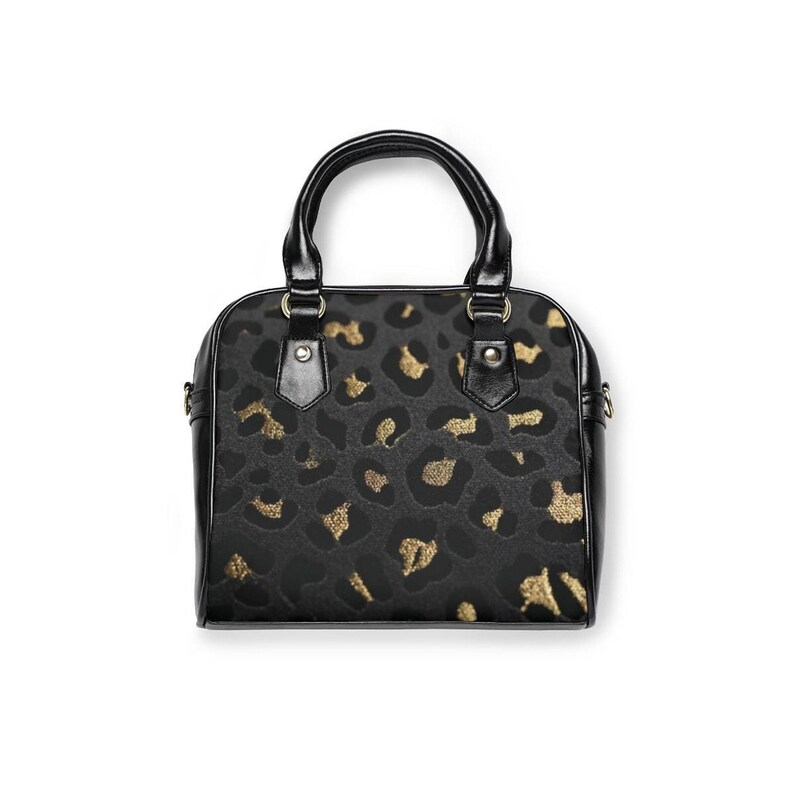 Front view of a structured small handbag with black leather handles and trim, featuring a grey and gold leopard print pattern against a white background.