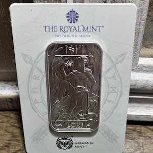 Puede incluir: Una barra de plata rectangular con una representación en relieve de la figura Loki, con el nombre LOKI inscrito en la parte inferior. La barra está montada sobre una tarjeta blanca etiquetada como THE ROYAL MINT y GERMANIA MINT con símbolos rúnicos.