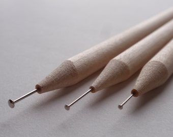 Op de afbeelding: Drie houten gereedschappen met metalen punten, gebruikt voor knutselen en het maken van gedetailleerde ontwerpen.
