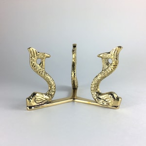 May include: A gold metal stand with three legs shaped like stylized seahorses. The stand is designed to hold a crystal ball or other round object.