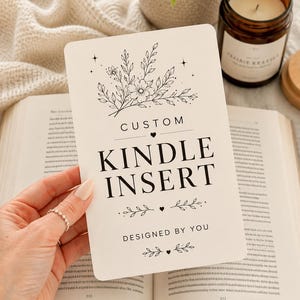 Op de afbeelding: Een rechthoekige witte kaart met afgeronde hoeken en zwarte tekst die luidt CUSTOM KINDLE INSERT DESIGNED BY YOU. Het ontwerp bevat zwarte lijntekeningen van bloemtakjes, kleine sterretjes en decoratieve krullen boven en onder de tekst.