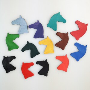 May include: A collection of 12 horse head shapes cut from leather and painted in various colours, including red, blue, green, yellow, black, brown, purple, and teal.