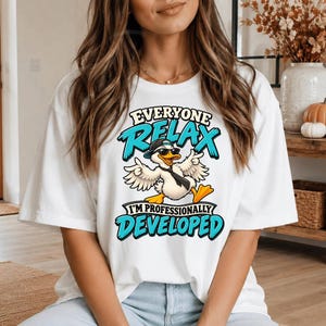 Könnte beinhalten: Ein weißes Kurzarm-T-Shirt mit einer Grafik einer weißen Ente, die eine schwarze Baseballkappe, eine Sonnenbrille und eine schwarze Krawatte trägt. Der Text lautet "EVERYONE RELAX I'M PROFESSIONALLY DEVELOPED" in blauer und schwarzer Schrift.