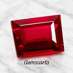 Peut inclure: Une pierre précieuse rouge rectangulaire à facettes avec un aspect vibrant et translucide et des bords nets. La pierre présente des teintes cramoisies profondes et des reflets lumineux internes. Le texte Gemscarts est imprimé en noir sous la pierre.