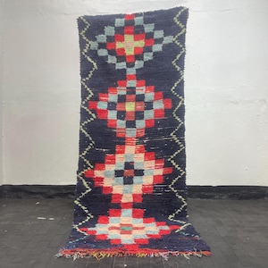 May include: A rectangular runner rug featuring a deep navy blue background with four large, vertically aligned diamond-shaped geometric patterns in red, light blue, and cream. The edges are framed by thin, light green zigzag lines.