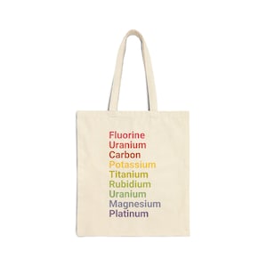 Puede incluir: Una bolsa de tela beige con una lista vertical de elementos químicos impresa en un degradado de arcoíris. El texto dice Fluorine, Uranium, Carbon, Potassium, Titanium, Rubidium, Uranium, Magnesium y Platinum en una fuente sans-serif simple.